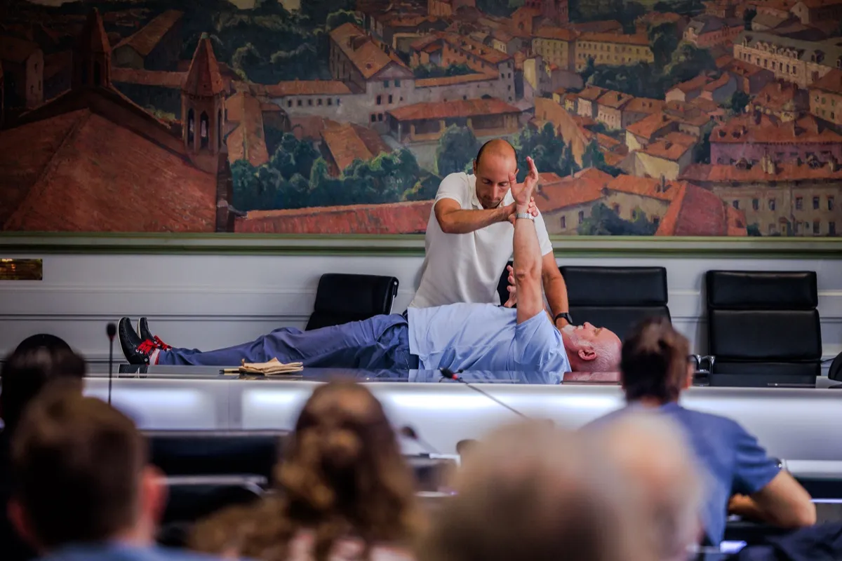 An instructor demonstrating an arm muscle test on a supine patient in front of a seminar audience