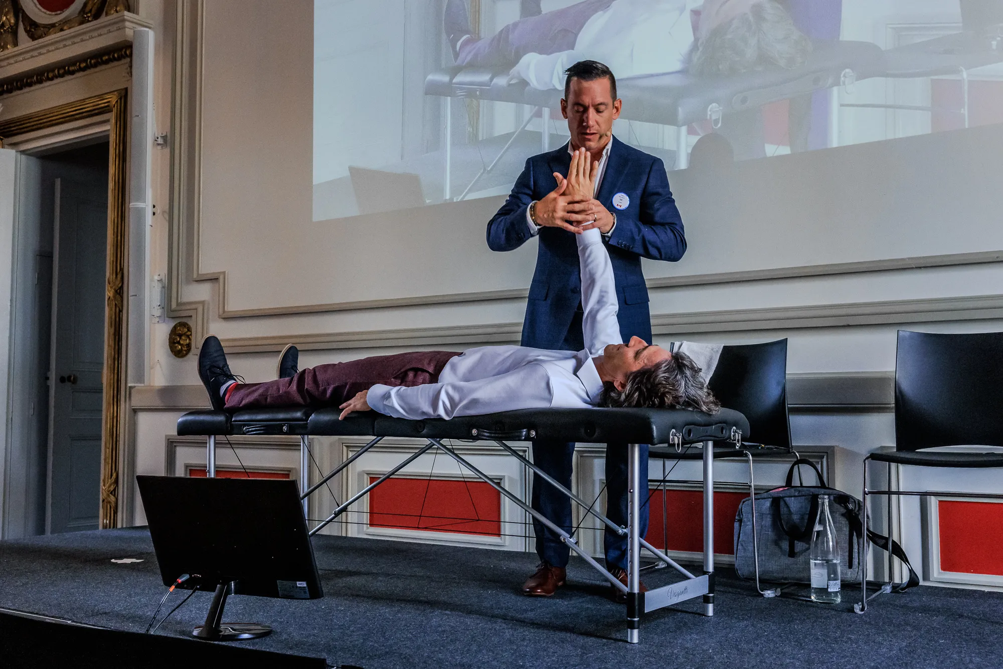 An ICAK instructor demonstrating a manual muscle test on stage at an international seminar