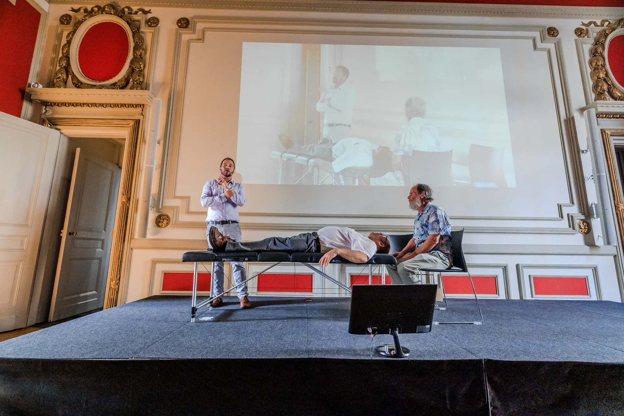 An ICAK seminar in session in a historic lecture hall, with a demonstration on stage