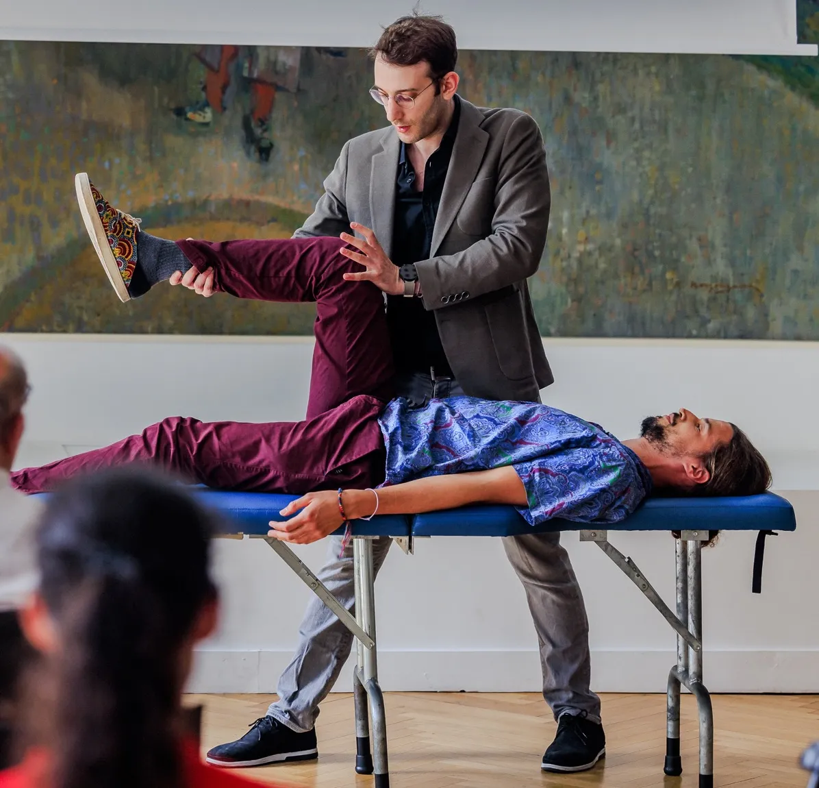 An ICAK practitioner performing a manual muscle test on a patient's leg in front of a seminar audience